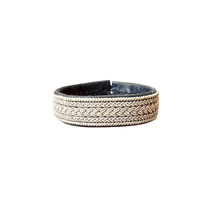 Handgjort brett armband i renskinn med täta tenntrådsflätor och renhornsknapp, inspirerat av Áhkká-massivet och en hyllning till starka kvinnor och nordiskt hantverk.