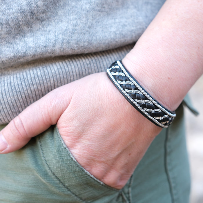 Handgjort armband i renskinn med tenntrådsfläta och renhornsknapp, inspirerat av Kebnekaise och fjällens kraftfulla landskap.