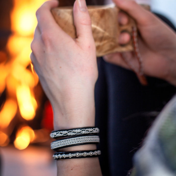 Handgjort armband i renskinn med klassisk tenntrådsfläta och renhornsknapp, inspirerat av vinter och nordisk enkelhet.