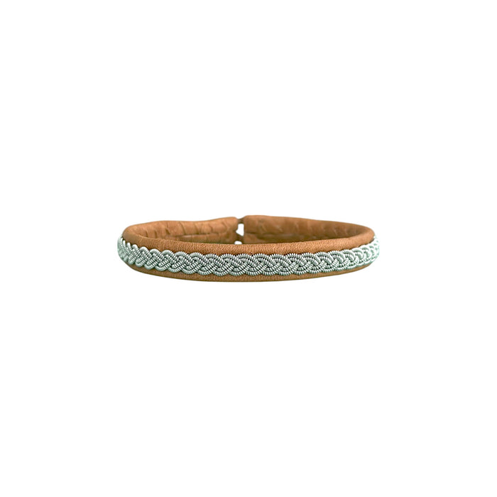 VINTER är ett handgjort armband i renskinn med traditionell tenntrådsfläta, inspirerat av vinter, samiskt arv och den nordiska naturens stillhet.