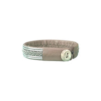 Handgjort armband i renskinn med tenntrådsfläta och renhornsknapp, inspirerat av frostens mönster och vinterns stillhet.
