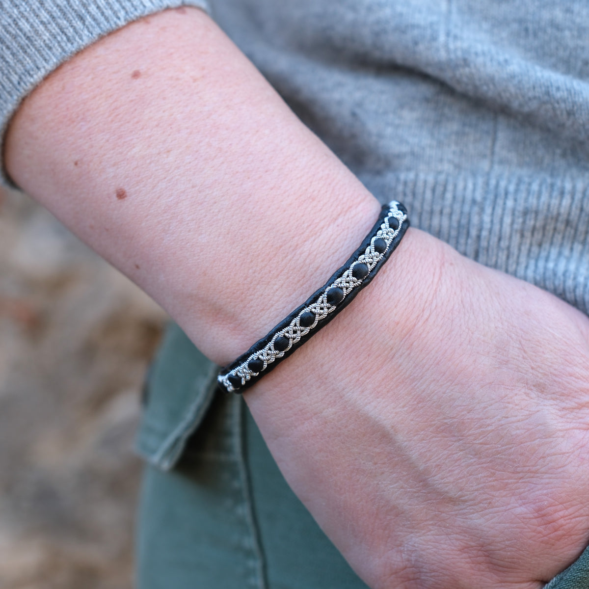 Handgjort smalt armband i renskinn med tenntrådsfläta och renhornsknapp, inspirerat av naturens lugn och nordisk enkelhet.