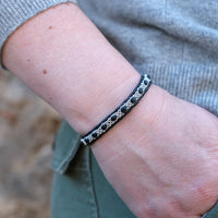 Handgjort smalt armband i renskinn med tenntrådsfläta och renhornsknapp, inspirerat av naturens lugn och nordisk enkelhet.