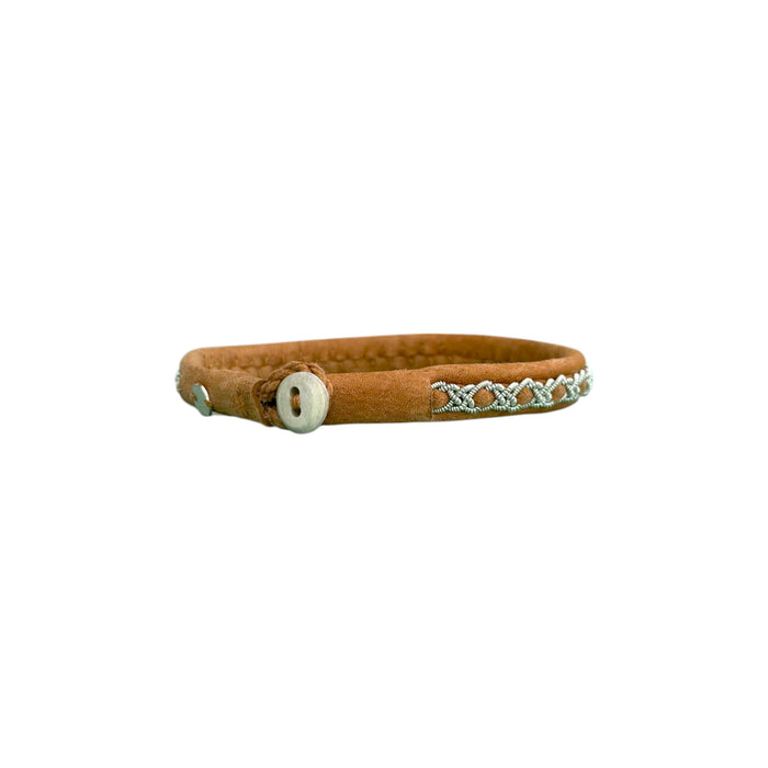 Handgjort smalt armband i renskinn med tenntrådsfläta och renhornsknapp, inspirerat av naturens lugn och nordisk enkelhet.
