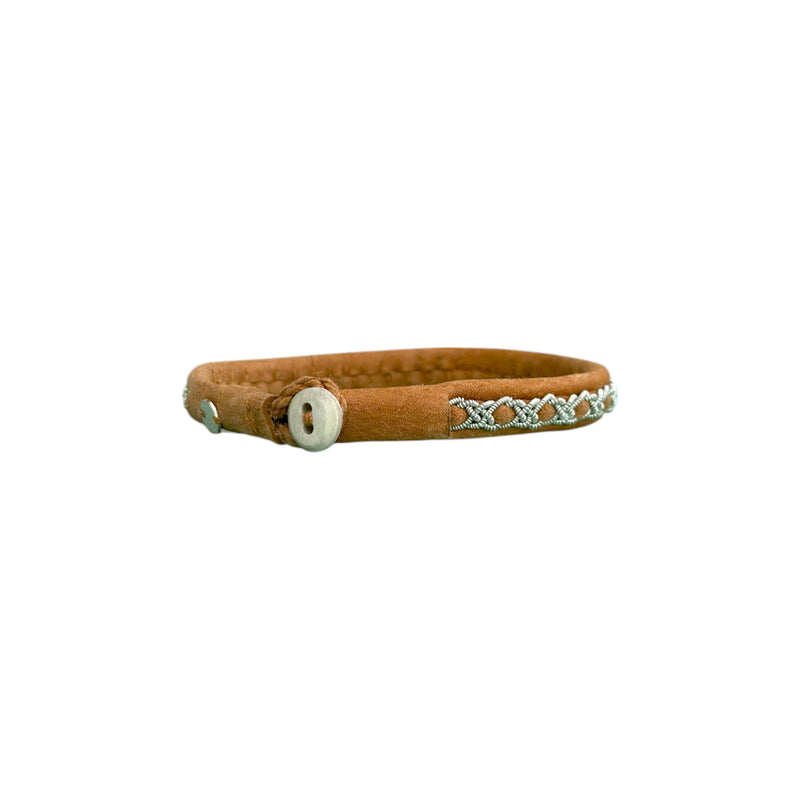 Handgjort smalt armband i renskinn med tenntrådsfläta och renhornsknapp, inspirerat av naturens lugn och nordisk enkelhet.

