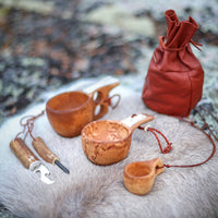 ett renskinn liggandes på en sten men tre olika kåsor, en kaffepåse i renskinn samt ett tändstål
