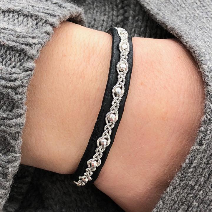 Handgjort armband i renskinn med tenntrådsfläta, dekorerat med silverpärlor och renhornsknapp, inspirerat av midnattssolens ljus över Lapplands fjäll.