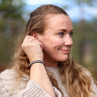 Tennarmband Polarnatt från Arctic Collection med handflätad tenntråd på en kvinnas handled. Kvinnan bär en naturvit stickad tröja och står utomhus i nordisk natur. Kopiera