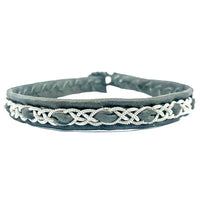 Närbild på tennarmbandet Snö från Arctic Collection, handgjort i mörkgrönt renskinn med silverfärgad tenntrådsfläta. Armbandet visas framifrån mot vit bakgrund