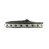 Närbild på tennarmbandet Snö från Arctic Collection, handgjort i mörkbrunt renskinn med silverfärgad tenntrådsfläta. Armbandet visas framifrån mot vit bakgrund