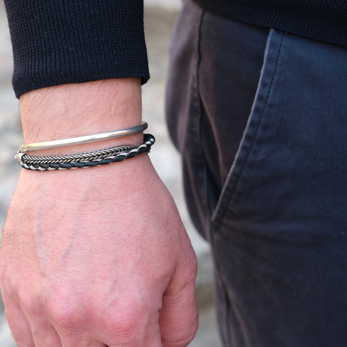 Handgjort smalt armband i renskinn med tenntrådsfläta och renhornsknapp, inspirerat av slingrande stigar i nordisk natur.