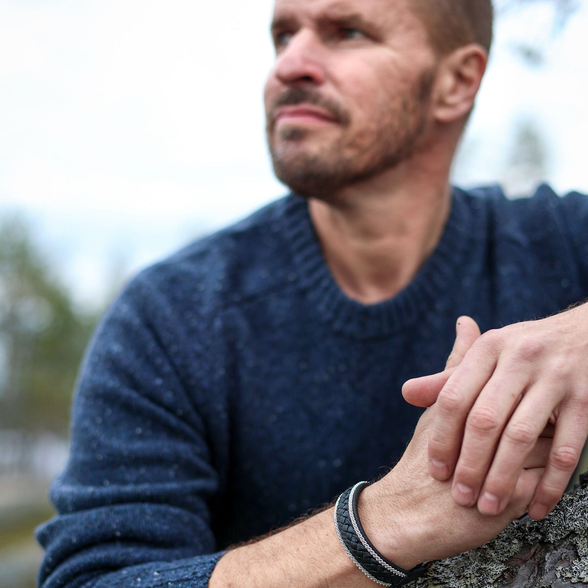 bredare armband i svart renskinn på en mans handled i blå tröja i naturen