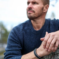 bredare armband i svart renskinn på en mans handled i blå tröja i naturen
