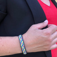 Tennarmband Tradition från Arctic Collection i svart renskinn med färgglad fläta av tenntråd. Armbandet bärs på en kvinnas handled tillsammans med en svart kavaj och röd topp. 