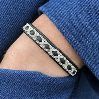 Handgjort armband i renskinn med tenntrådsfläta och renhornsknapp, inspirerat av nordisk vildmark.
