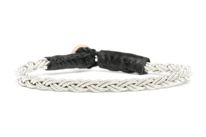 Handgjort armband i renskinn med tenntrådsfläta och renhornsknapp, inspirerat av stigar och leder i nordisk natur.