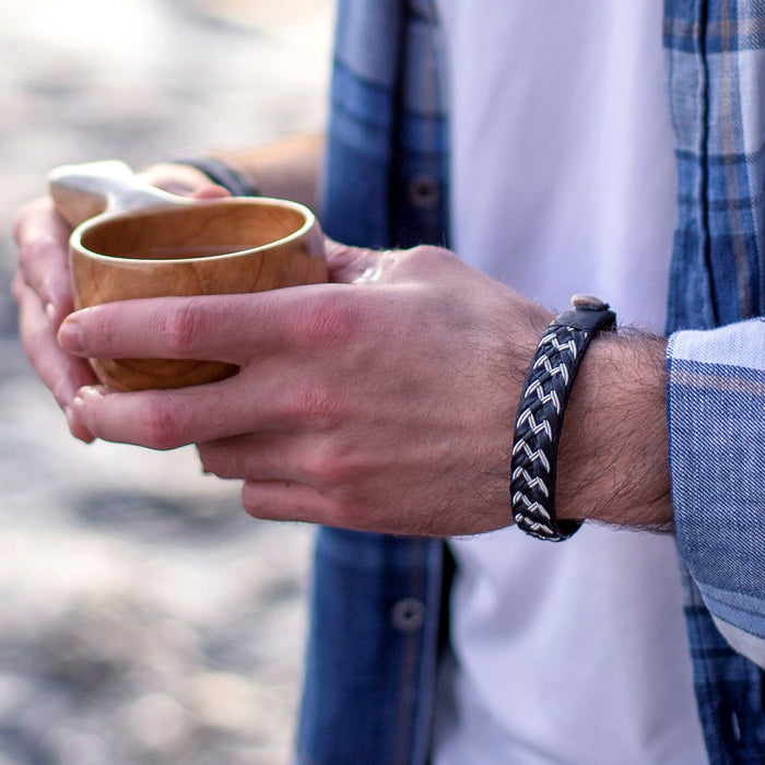 Handgjort armband i renskinn med sicksackmönstrad tenntrådsfläta och renhornsknapp, inspirerat av Muddus nationalpark.